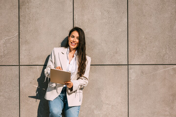 Portrait of a smiling business woman using digital tablet during quick break in front a corporate building.