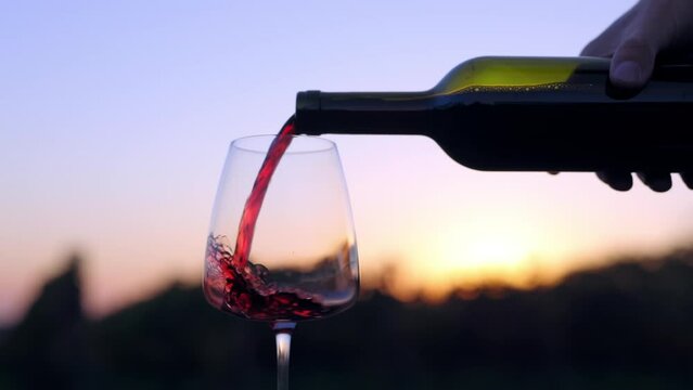 A man pours red wine into a glass after sunset