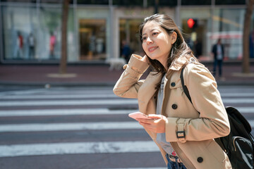 asian Japanese girl traveler holding blowing hair and looking into space with smile and phone in hand while waiting for bus on street in downtown san Francisco California usa