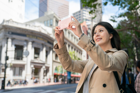 happy asian Japanese female tourist taking picture of the beautiful city with her mobile phone on the corner of street in san Francisco California usa