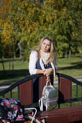 The girl stands near the bench in the autumn park and smiles. Dressed in autumn clothes. Autumn city park.