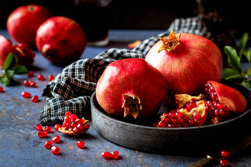 Red ripe pomegranates  on a dark plate with split open parts showing the clusters of juicy seeds