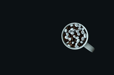 Dark brown and white coffee beans in a cup on black background flat lay with copy space. Cappuccino or latte concept.