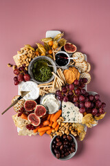 Top down view of a beautifu vegetarian cheese platter board on pink background