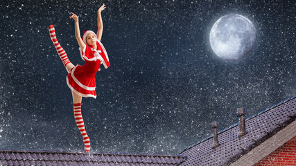 Dancing girl ballerina with a gift in her hands in a Santa Claus costume on the roof of a house on Christmas night against the background of the starry sky. © Maria Moroz
