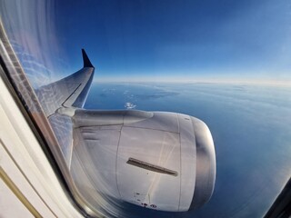 A view of blue sky through airplane window during flight. View from airplane window with wing and engine during flight in the air