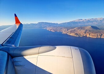 A view of Crete shore through airplane window during landing. View from airplane window with wing and engine during landing to Crete, Greece