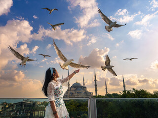 Obraz premium Lifestyle, Asian woman tourist feeding seagulls at view point in vacation. There is a Blue Mosque in the background in a blur. Popular tourist destination. Sultanahmet, Istanbul, Turkiye, Turkey