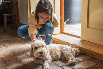 Child girl 10 years old gently stroking a fluffy beige dog squatting on the threshold of the country house