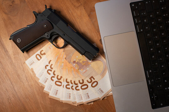 liasse de billets de 50 euros posés sur une table à côté d'un ordinateur portable. Une arme est posée sur l'argent.