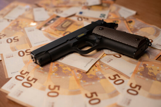 un pistolet est posé sur un gros tas de billets de banques qui recouvre l'ensemble de l'image