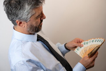 Un homme d'affaires de 50 ans tient une liasse de billets de banque dans ses mains et compte son argent. Concept du profit et du succès dans les affaires - obrazy, fototapety, plakaty
