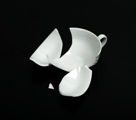 Broken white cup on black Background.  An empty cup is broken into pieces.Broken Cup.                                                