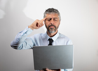 homme d'affaires de 50 ans tenant un ordinateur portable en train de réfléchir et d'essayer de trouver une solution pour résoudre un problème.