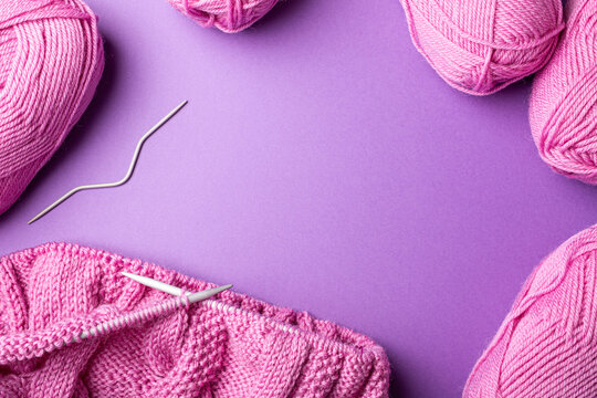 Knitting flat lay with pink wool yarn and knit accessories over lilac, top view, overhead shot with copy space