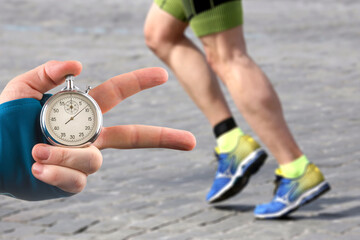 measuring the running speed of an athlete using a mechanical stopwatch. hand with a stopwatch on the background of the legs of a runner