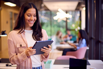 Fototapeta premium Smiling Businesswoman Standing In Modern Open Plan Office Using Digital Tablet