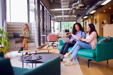 Businesswomen Having Informal Meeting In Breakout Seating Area Of Modern Office