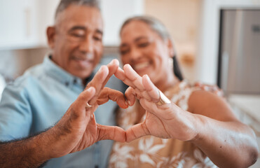 Hands, heart and love with a senior couple in their retirement home together for health, wellness and romance. Fingers, sign and affection with a mature man and woman pensioner bonding in their house