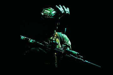 Modern army special forces equipped soldier, anti terrorist squad fighter, elite mercenary armed assault rifle, standing in darkness with night vision goggles on helmet, studio portrait, green light