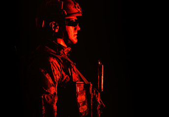 Half length low angle studio shot of special forces soldier in field uniforms with weapons, portrait on black background. Protective goggles glasses are on