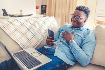 Shot of a young man using a laptop while relaxing on a sofa. Young African American using laptop on couch.