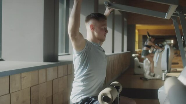 Muscular man in sportswear using lat pulldown machine while training in gym