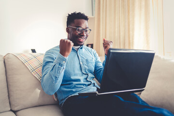 Happy young businessman using laptop at home. Young man working on computer at home. Casual entrepreneur feeling excited about new project while working on laptop at home.
