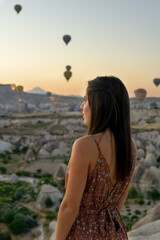 Young woman enjoying the view of the hot air balloons flying at sunrise in Cappadocia, Turkey.