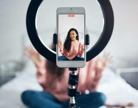 Live streaming, phone and black woman talking on video podcast in the bedroom of her house. Happy and excited girl or influencer speaking on the internet or social media with a mobile and ring light