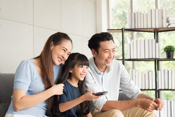 Happy mother father and daughter family sitting on couch and watching television together relaxing at home.