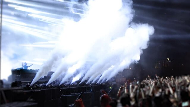 Fireworks and smoke blowing on night concert stage with flashing lights exiting fans
