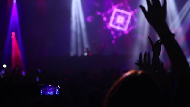 People with raised hands on music live event with lights, back view shot in slow motion