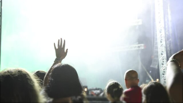 Outdoor summer night rock concert with flashing lights stage, people cheer and clap their hands in unison 