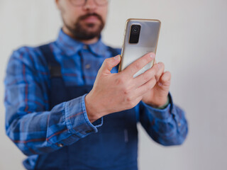 young man in blue work suit doing Repair apartment. Home renovation concept. Guy with smartphone texting and tapping on cellphone, searching for solution on Internet, ordering goods for repairs