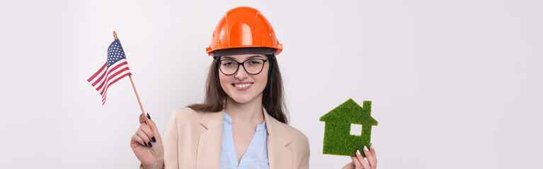 A girl in a construction helmet and an American flag holds a green eco house.