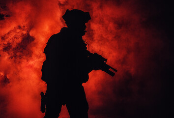 Silhouette of modern infantry soldier, elite army fighter in tactical ammunition and helmet, standing with assault service rifle in hands in the fire and smoke