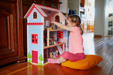 Adorable preschooler girl having fun with doll house in playroom at home