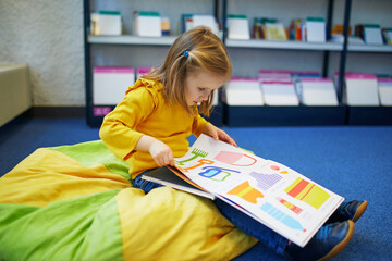 4 year old girl sitting on the floor in municipal library and reading a book