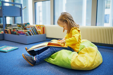 4 year old girl sitting on the floor in municipal library and reading a book