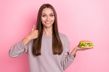 Photo of charming cheerful person hold burger demonstrate thumb up isolated on pink color background