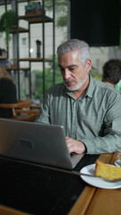 Older entrepreneur seated at coffee shop with laptop staring at screen. Closeup male senior executive working remotely using computer at cafe place in Vertical Video SS