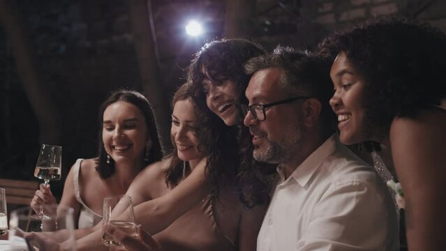 Modern ethnically diverse lesbian newlyweds enjoying their wedding party taking selfies with relatives and friends