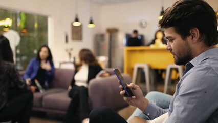 Young man looking at smartphone device in resting room at workplace. Person browsing internet social media on phone at office place