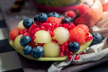 Composition of fresh fruit. Fruit salad with pomegranate, melon, watermelon and blueberries. Hollow and ball-shaped fruits of watermelon and melon.