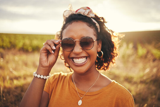 Face, Fashion And Nature With A Black Woman Outdoor On A Field With Green Grass In Sunglasses And A Smile. Happy, Vacation And Summer With A Young Female Standing Outside Against A Sky Background