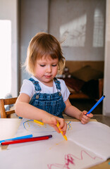 Small child at home at the children's table draws with felt-tip pens.