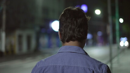 Back of a pensive thoughtful youn man walking in city street sidewalk at night