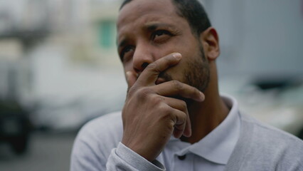 Naklejka premium Anxious young man feeling despair and negative thoughts. African American person suffering from mental illness standing in street covering face with hand