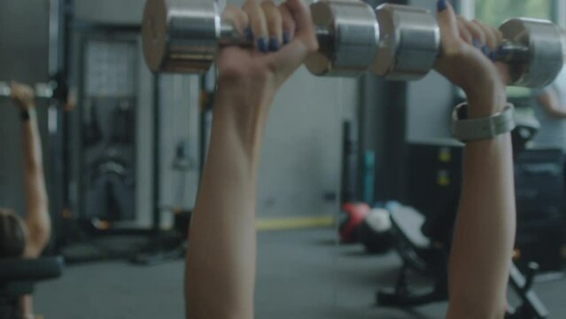 Close up handheld camera shot sporty woman doing dumbbell chest press exercise on bench while working out in gym